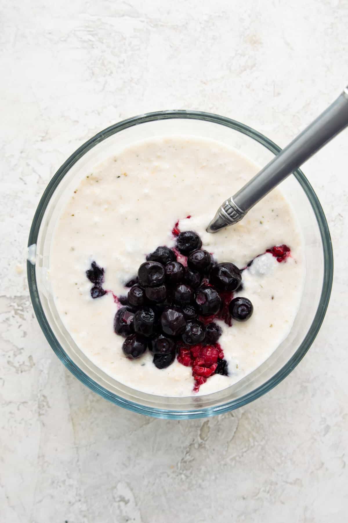 A bowl of overnight oats topped with fresh blueberries and with a spoon in it.