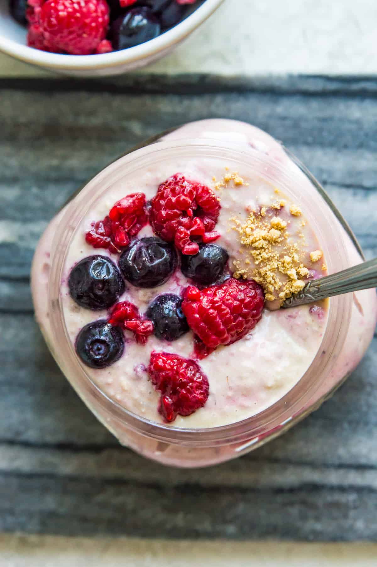 A bowl of berry cheesecake overnight oats topped with fresh berries and with a spoon in it.