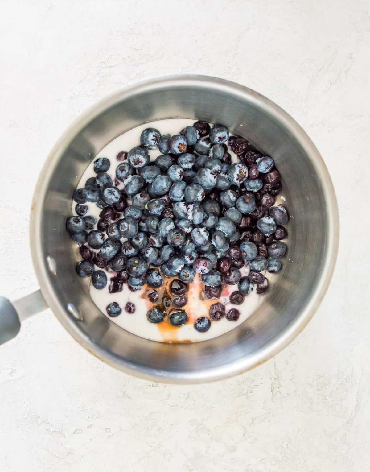 Blueberries, coconut milk and vanilla extract in a pot.
