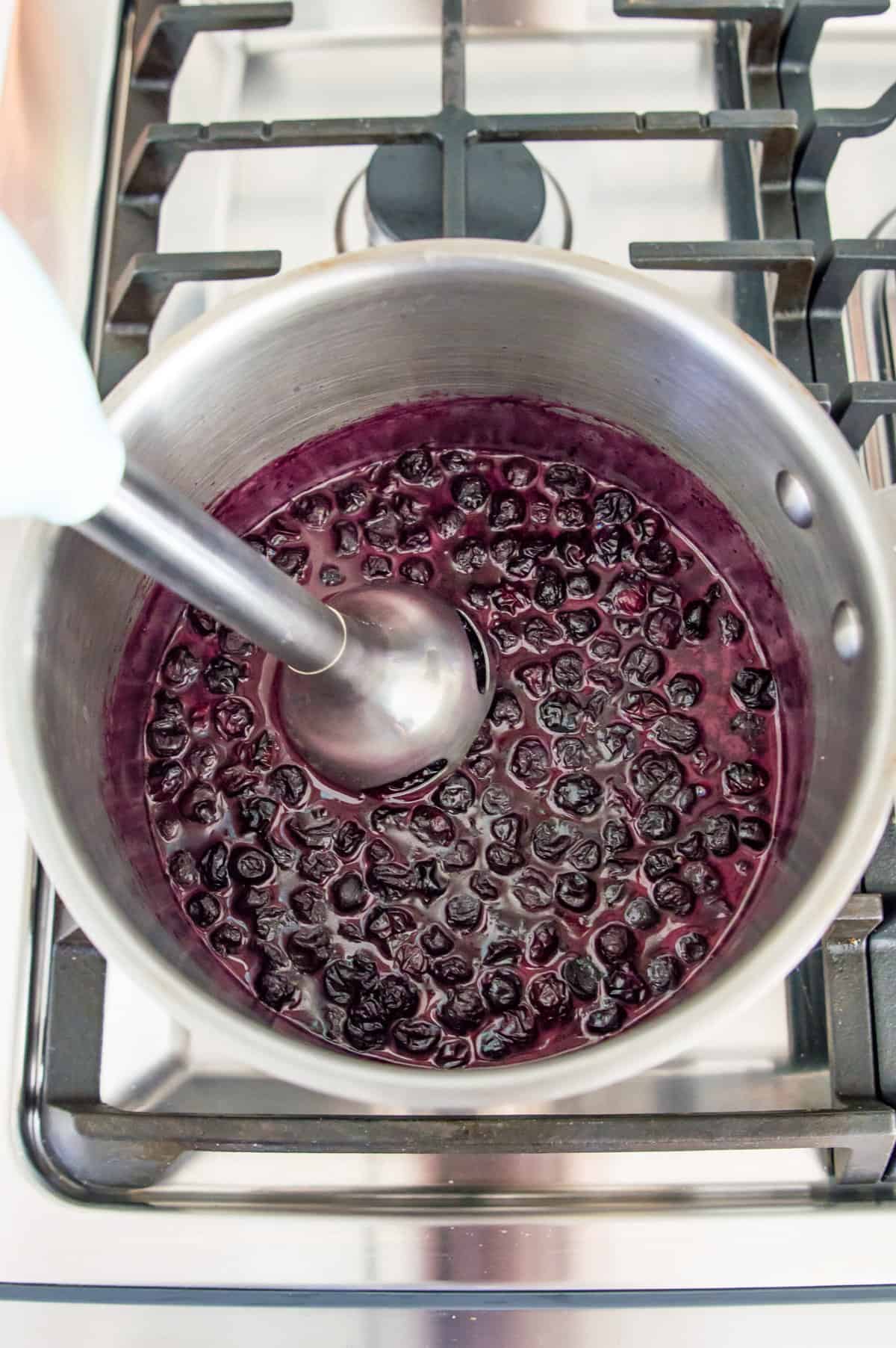 Cooked blueberries in a pot with an immersion blender in it.