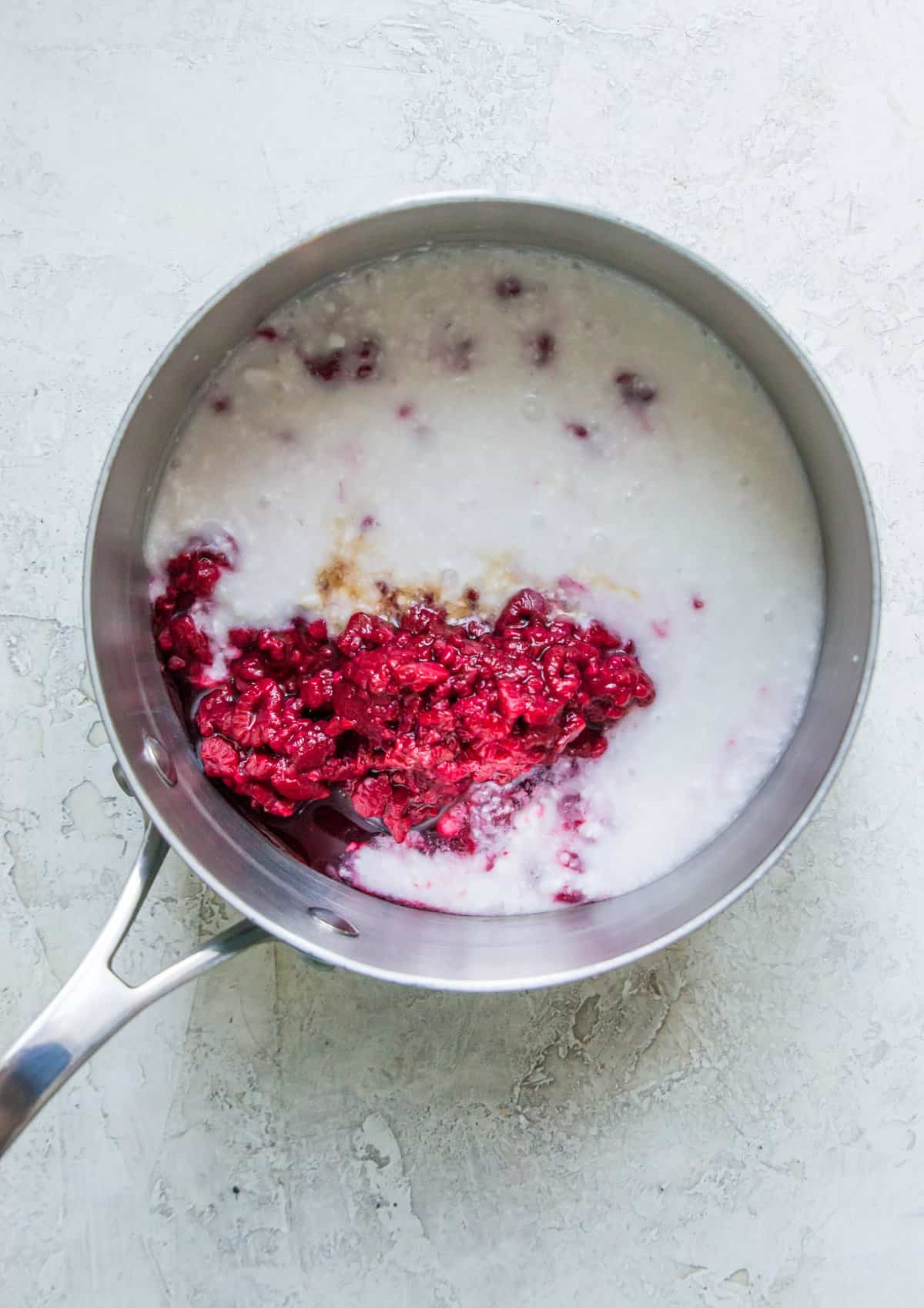 Coconut milk, maple syrup and raspberries in a pot.