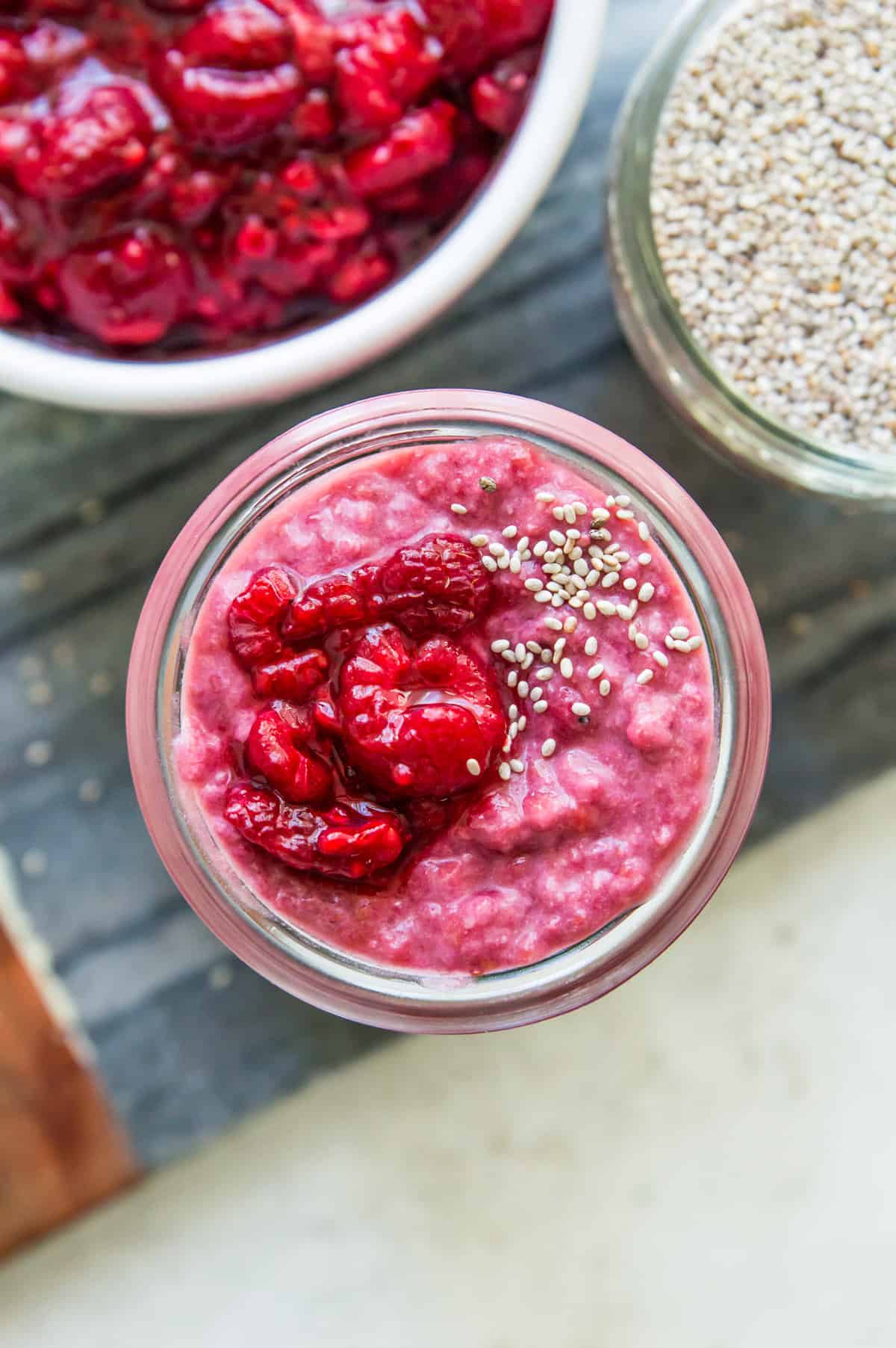 A jar of raspberry chia seed pudding topped with fresh raspberries and white chia seeds.