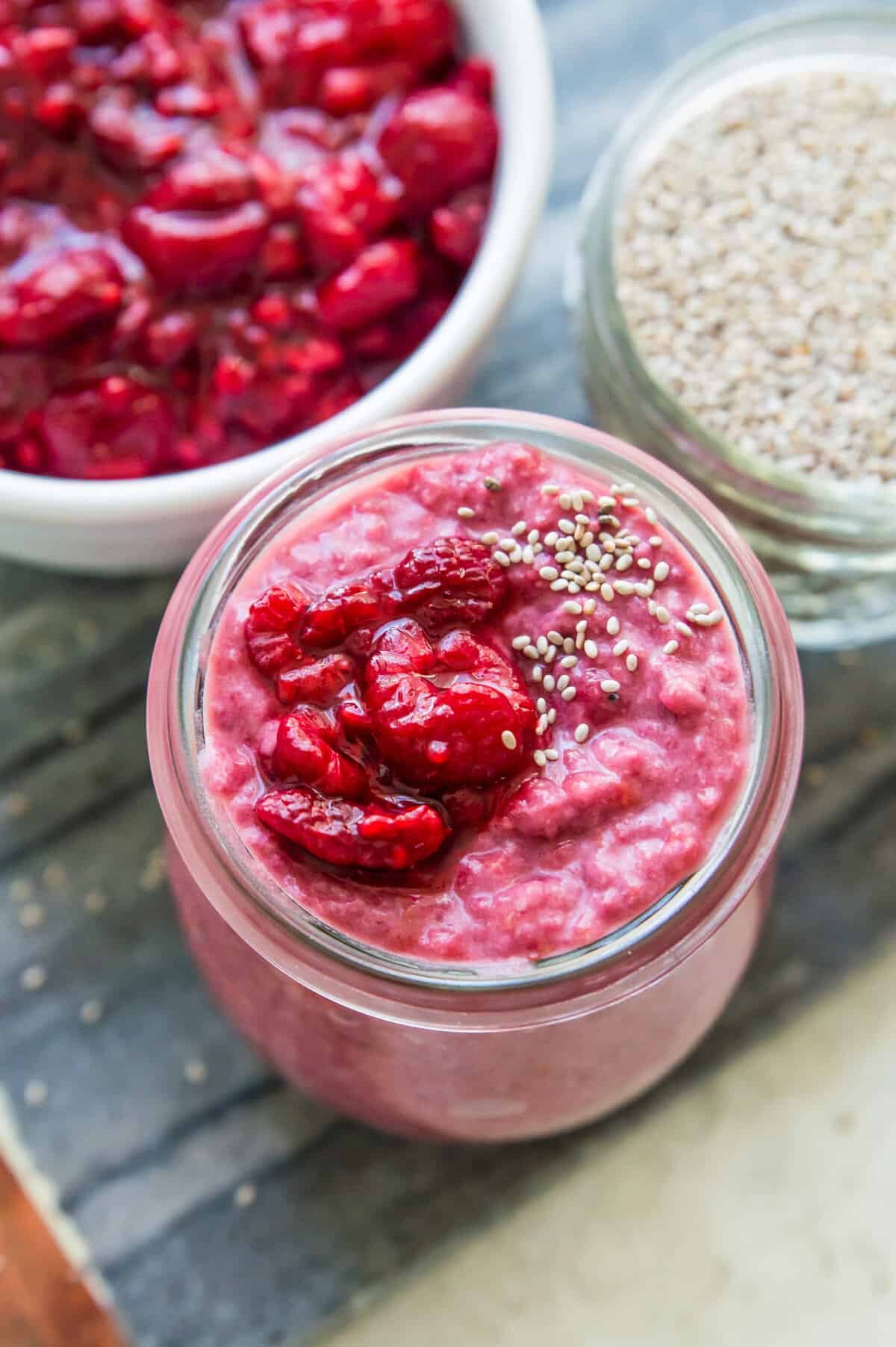 A jar of pink chia pudding topped with fresh raspberries and white chia seeds.