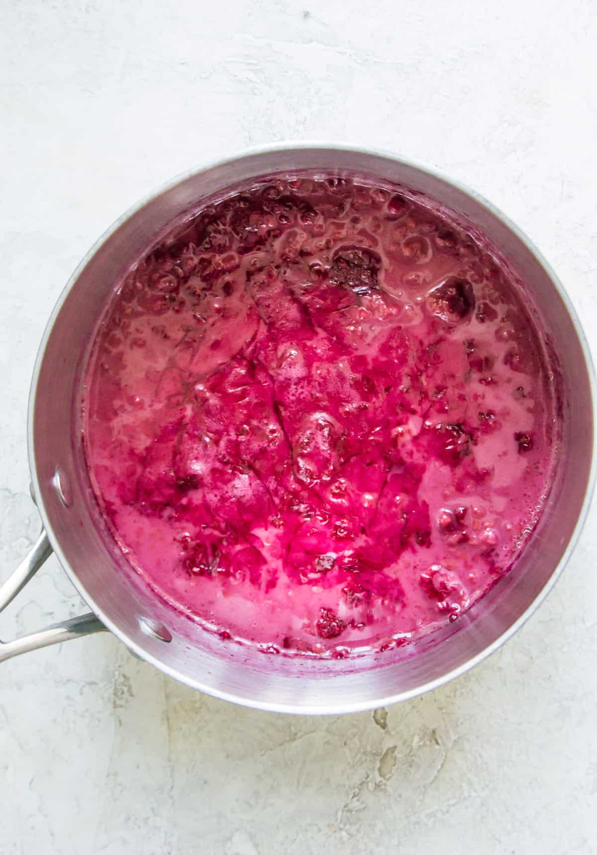 Coconut milk and raspberries that have been simmered together to make a thick, pink sauce in a pot.