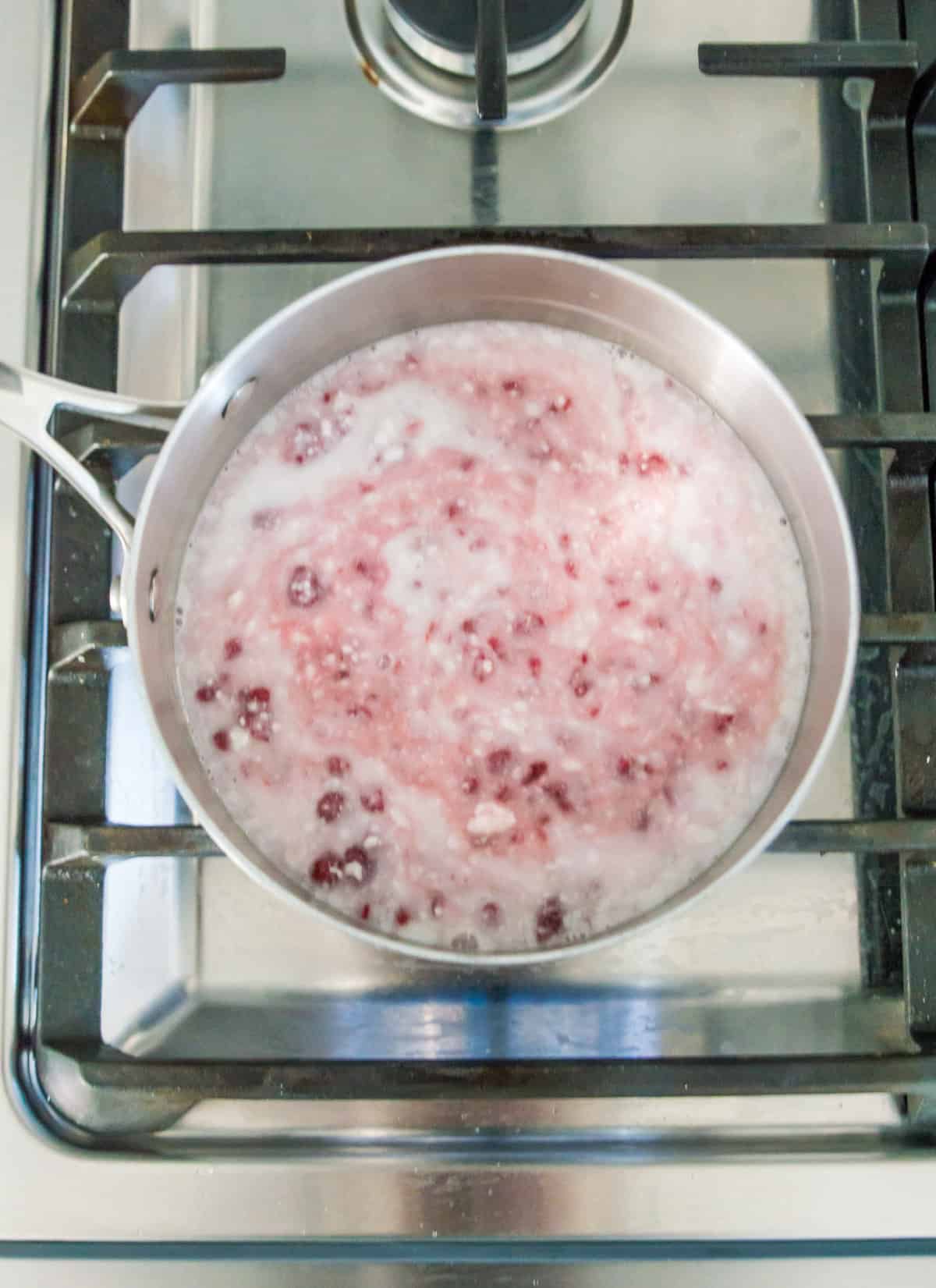 Coconut milk and raspberries in a pot, simmering on the stovetop.