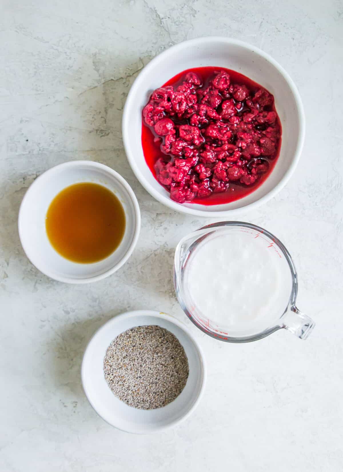 The ingredients needed to make a raspberry chia seed pudding separated into small bowls. 