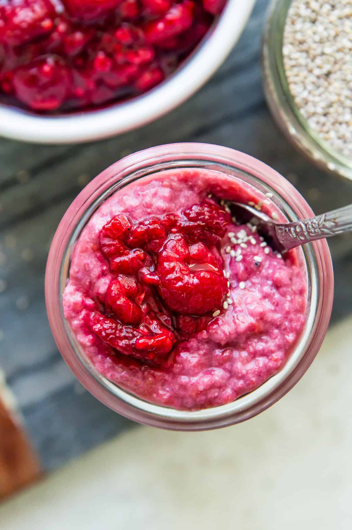 A jar of raspberry chia pudding topped with fresh raspberries and white chia seeds.