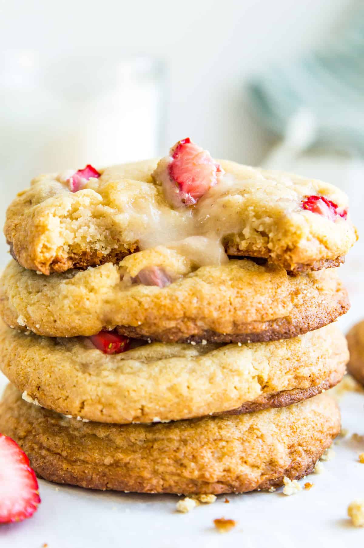 A stack of cheesecake filled strawberry cookies with fresh strawberries around them.