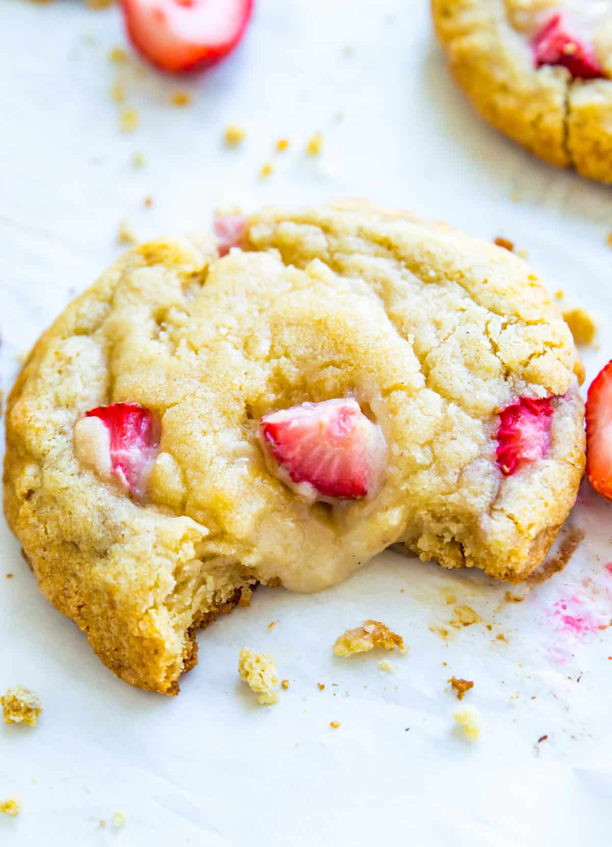 A strawberry cheesecake cookie on a baking sheet with cookie crumbs around it.