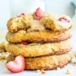 A stack of strawberry cheesecake cookies with fresh strawberries around them.