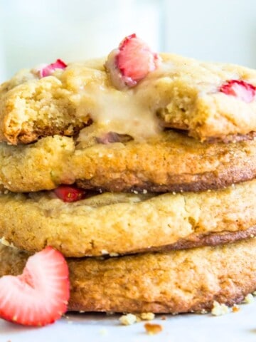 A stack of strawberry cheesecake cookies with fresh strawberries around them.
