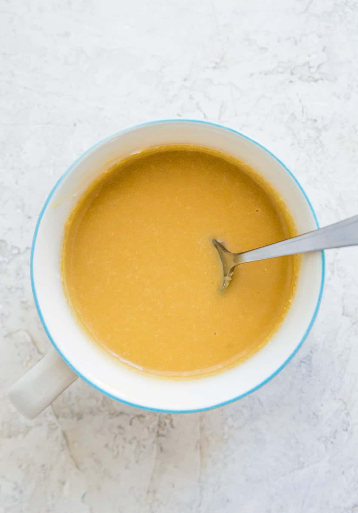 Batter to make a vanilla mug cake in a mug with a spoon in it.