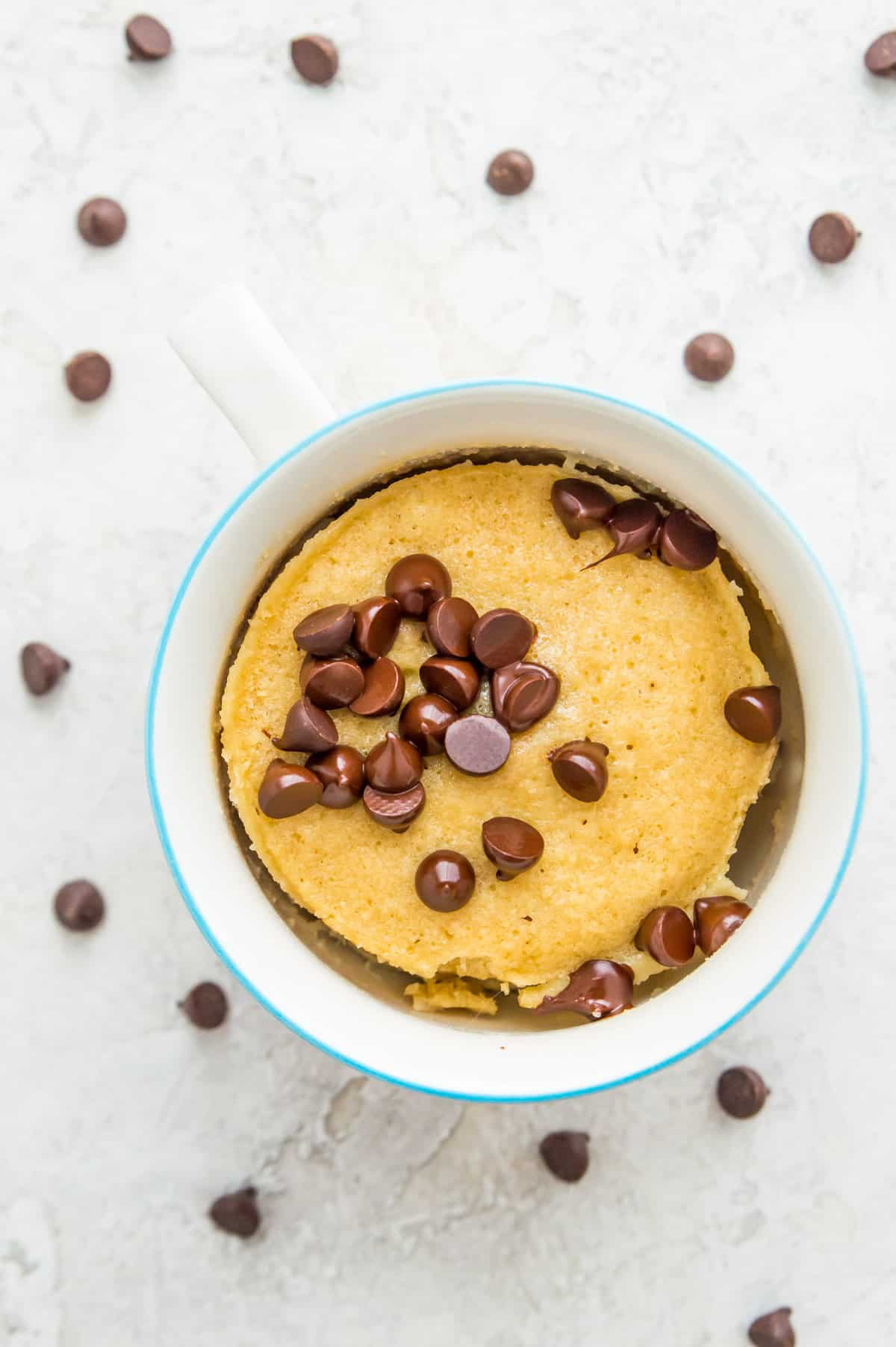 A cooked vanilla mug cake in a mug topped with chocolate chips that are starting to melt. 