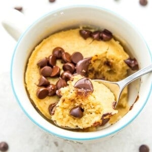 A mug of a vanilla protein mug cake with chocolate chips on top of it and a spoon in it.