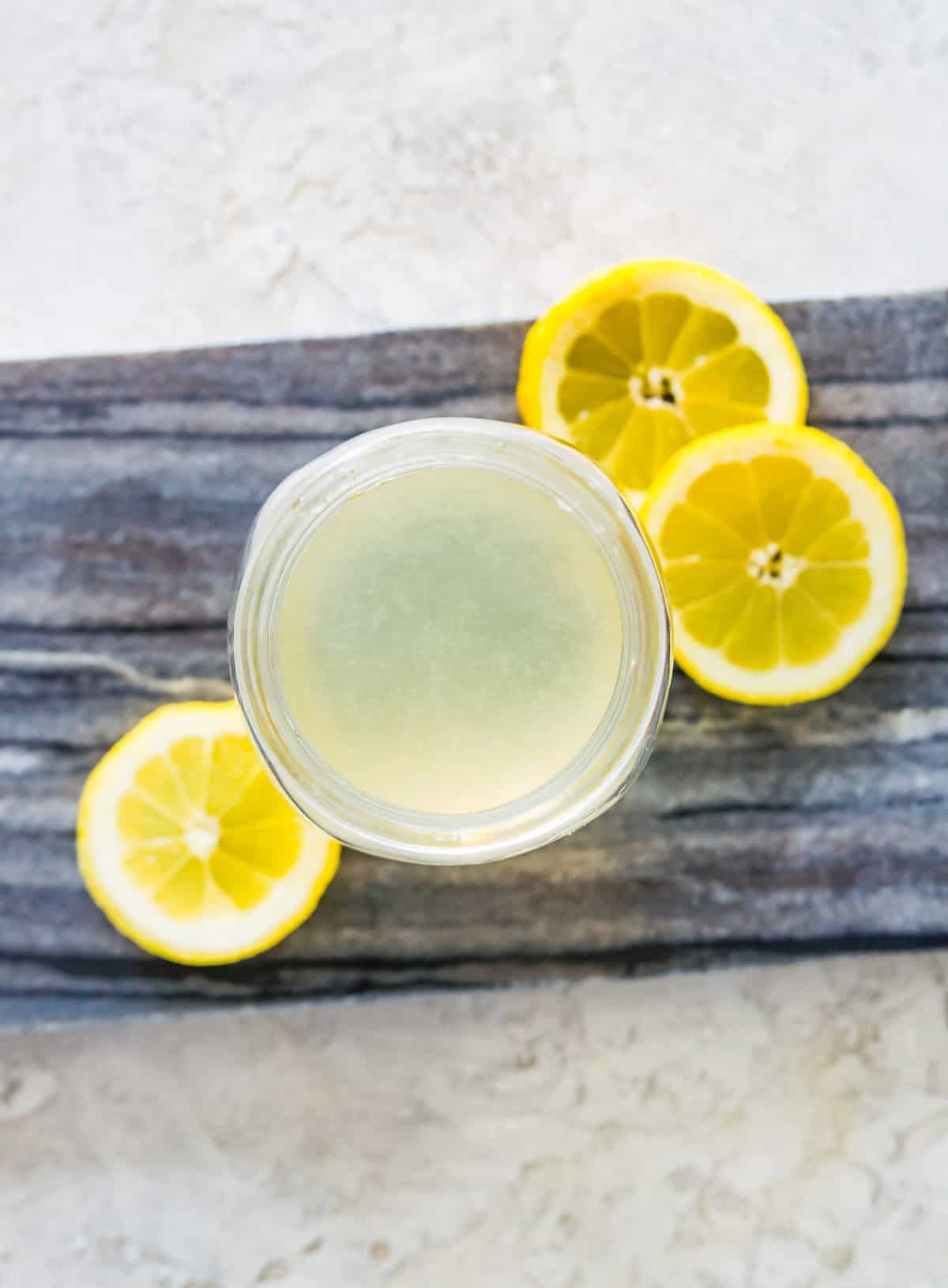 A jar full of water and lemon juice surrounded by lemon slices.