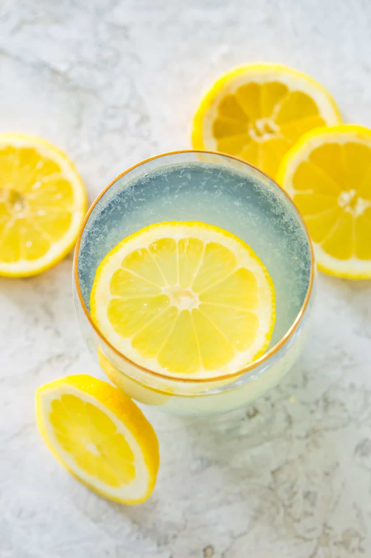 A glass of lemon water with a lemon slice in it and surrounded by more lemon slices.
