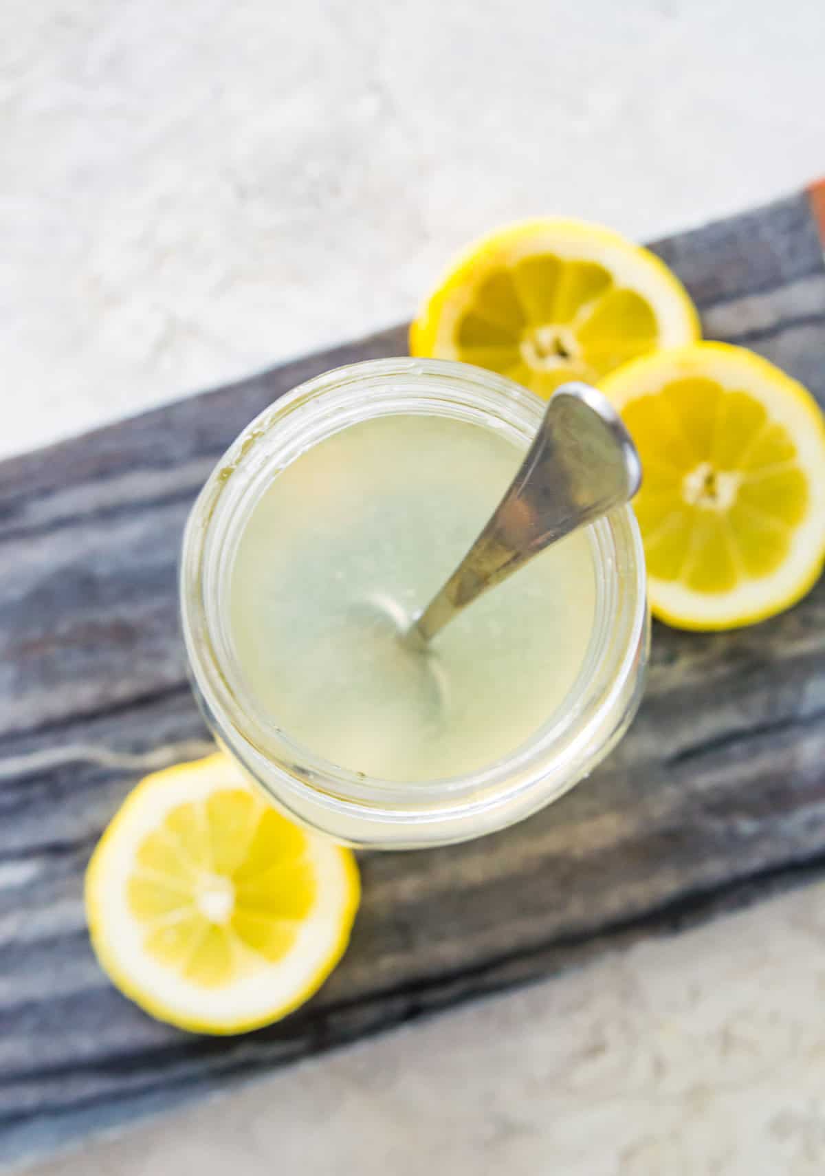 A glass jar filled with water and lemon juice with a spoon in it.