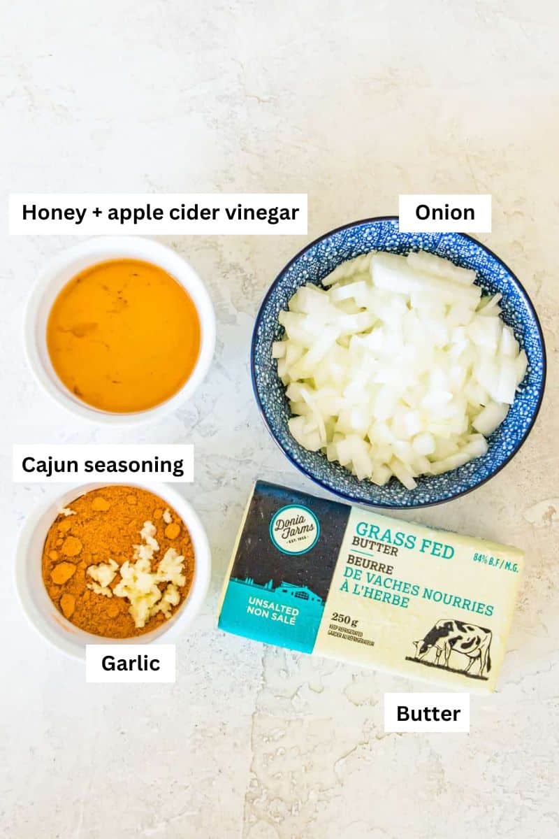 Bowls filled with different ingredients including honey, chopped onion, garlic, cajun seasoning and a stick of butter beside the bowls.