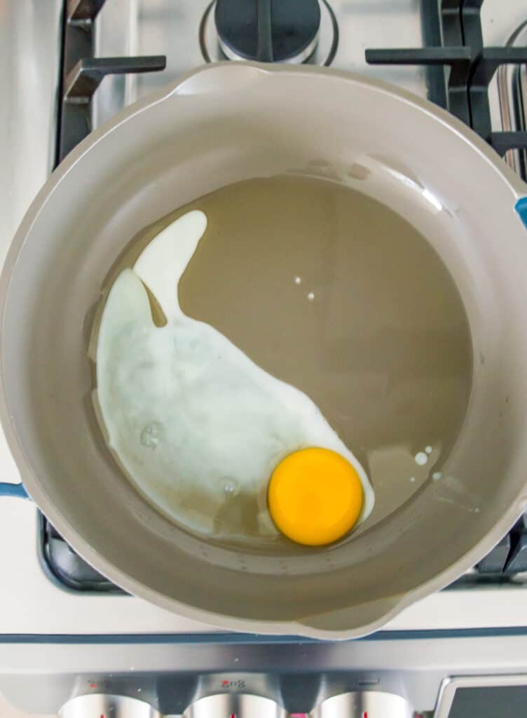 A pan on the stovetop with an egg cooking in it.