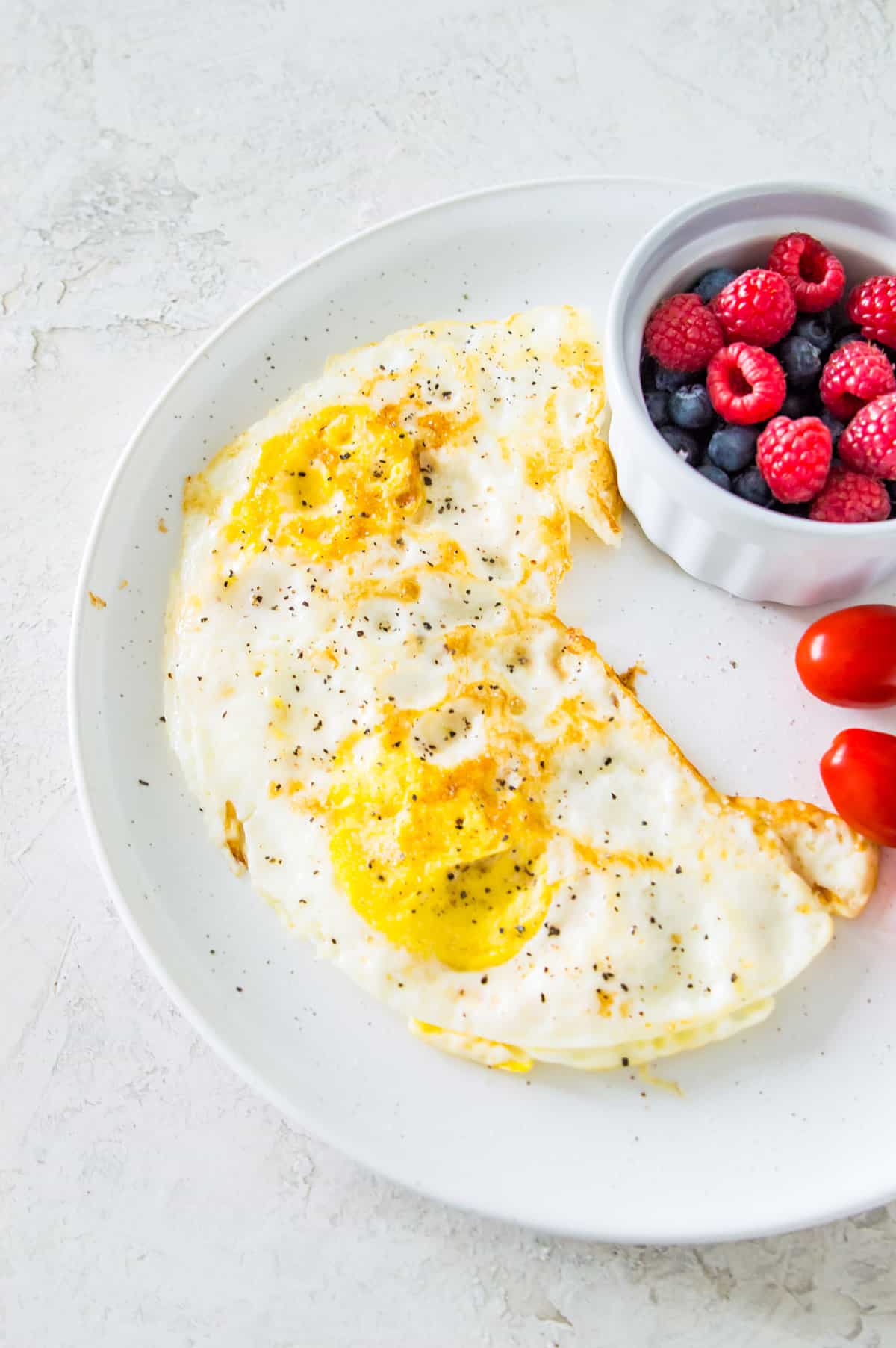 A plate with two over hard eggs on it seasoned with salt and pepper and with a side of baby tomatoes.