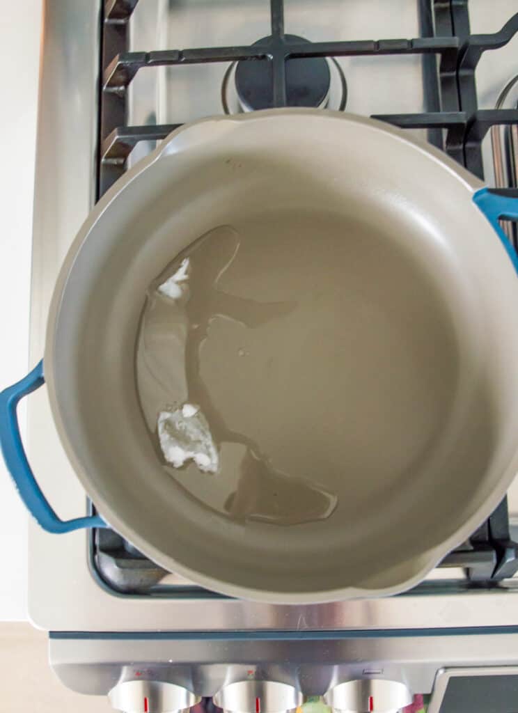 A pan on the stovetop with coconut oil melting in it.