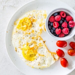 A plate with over hard eggs on it and a small bowl of blueberries and raspberries.