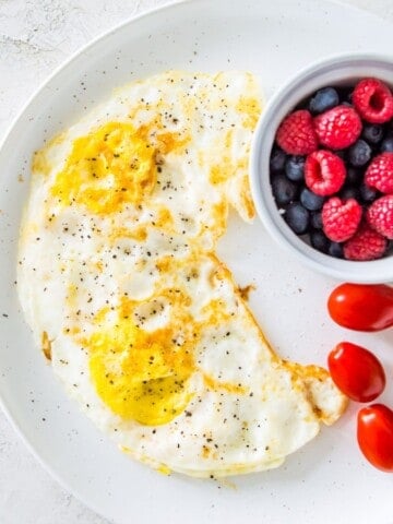 A plate with over hard eggs on it and a small bowl of blueberries and raspberries.