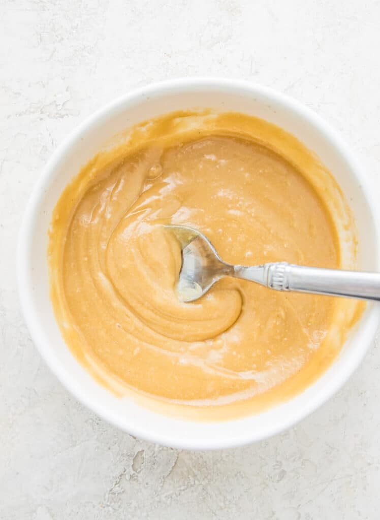 A bowl with a caramel sauce in it with a spoon in the caramel.