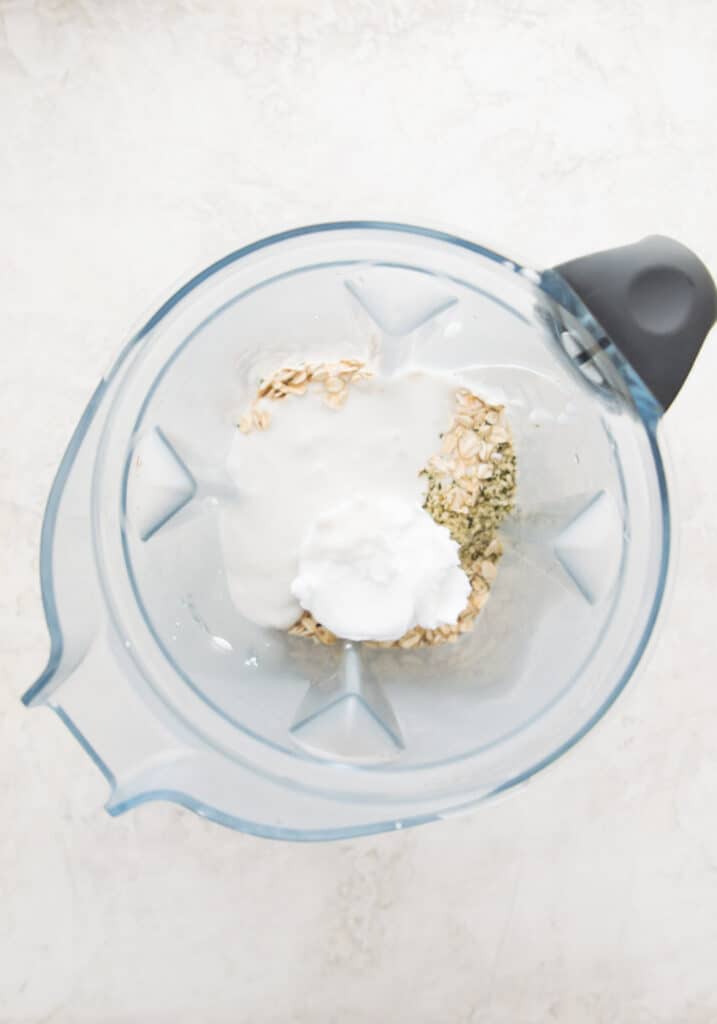 A blender with cream cheese, oats, milk, and hemp seeds in it.