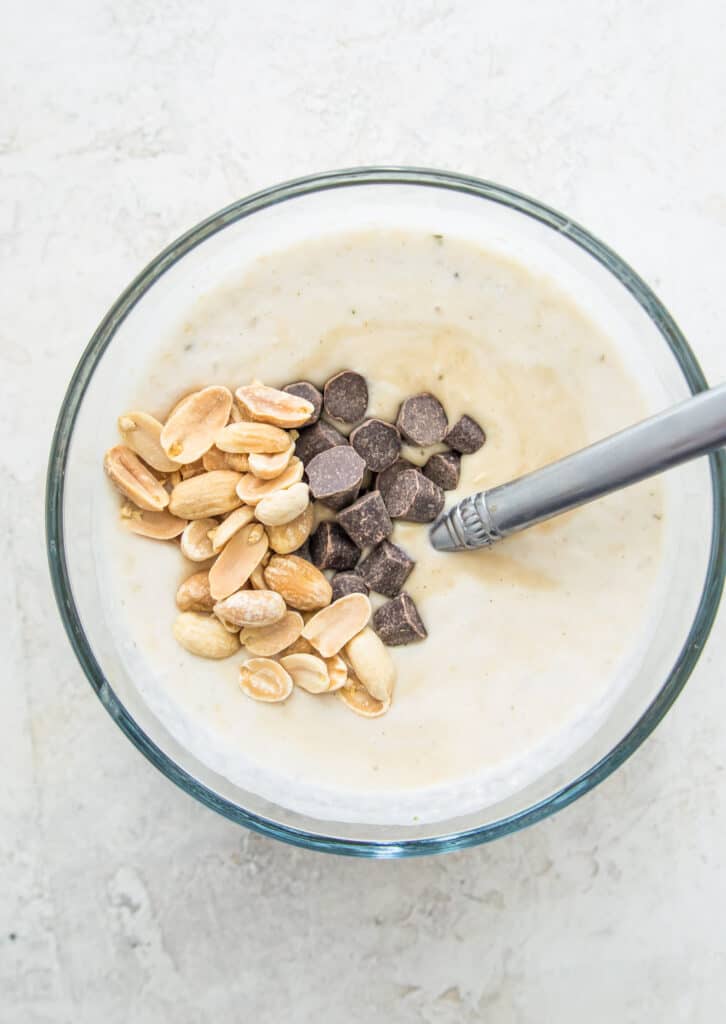 A glass bowl with peanuts, chocolate chips and milk in it.