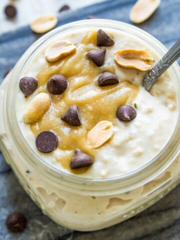 A jar of snickers cheesecake overnight oats topped with caramel sauce, peanuts and chocolate chips.