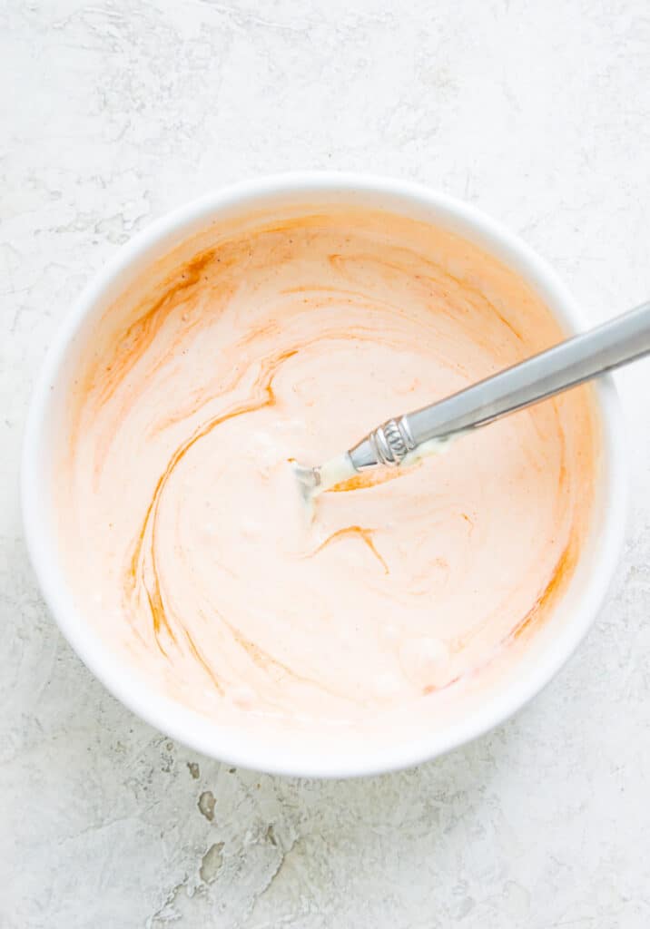 A bowl with a sriracha aioli sauce in it with a spoon in it.