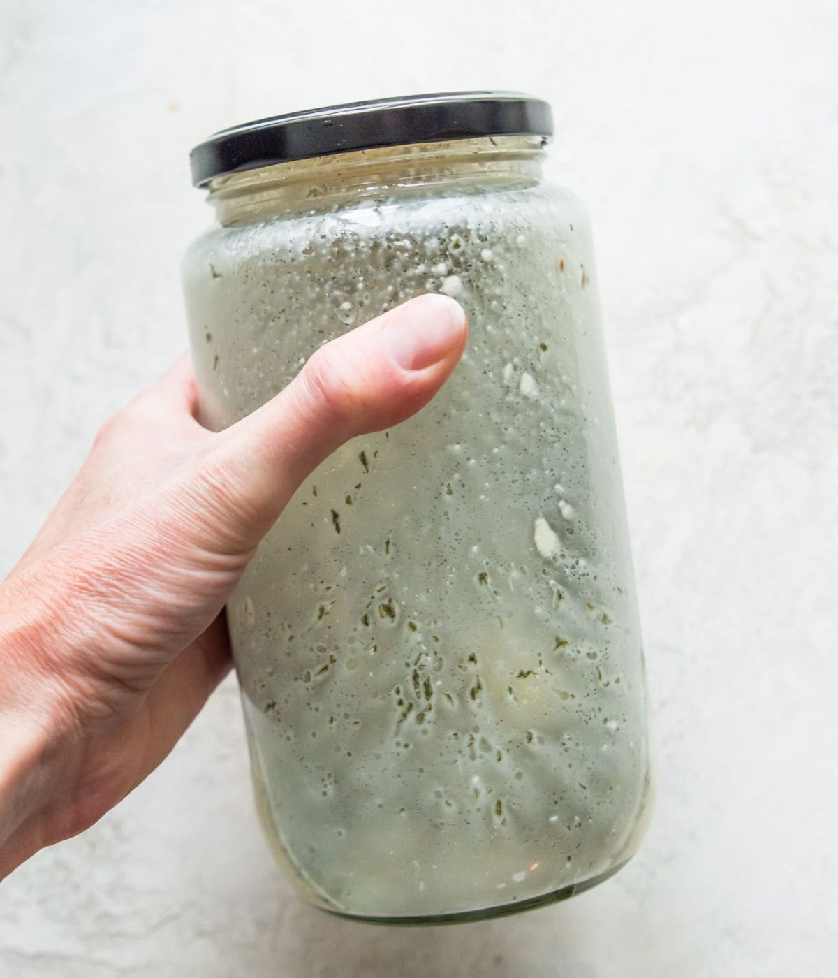A hand holding a jar with dressing in it with the lid on.