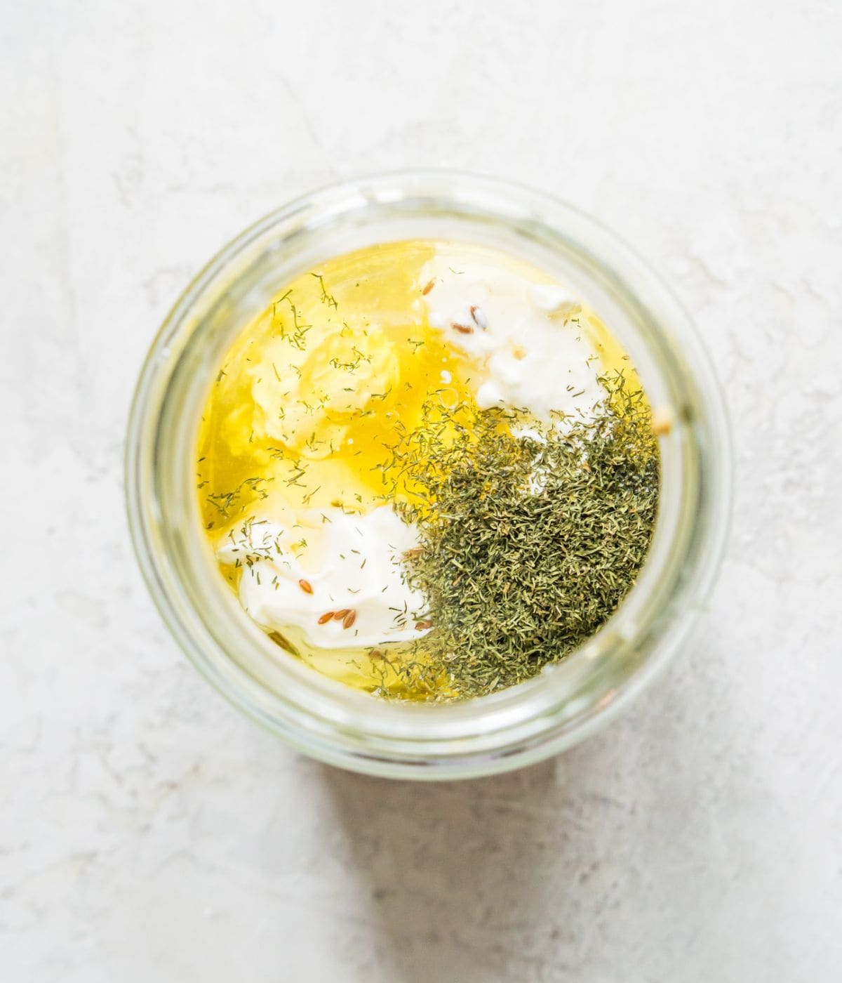 A jar with oil, mayonnaise, dried dill and honey in it.