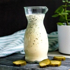 A bottle of dill pickle salad dressing with cut up pickles beside it.