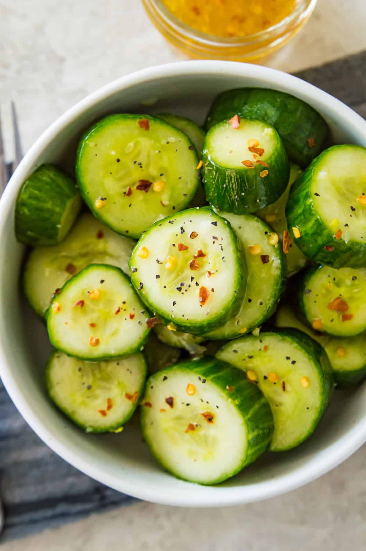 A bowl of an asian cucumber salad topped with chili flakes and with a fork beside it.