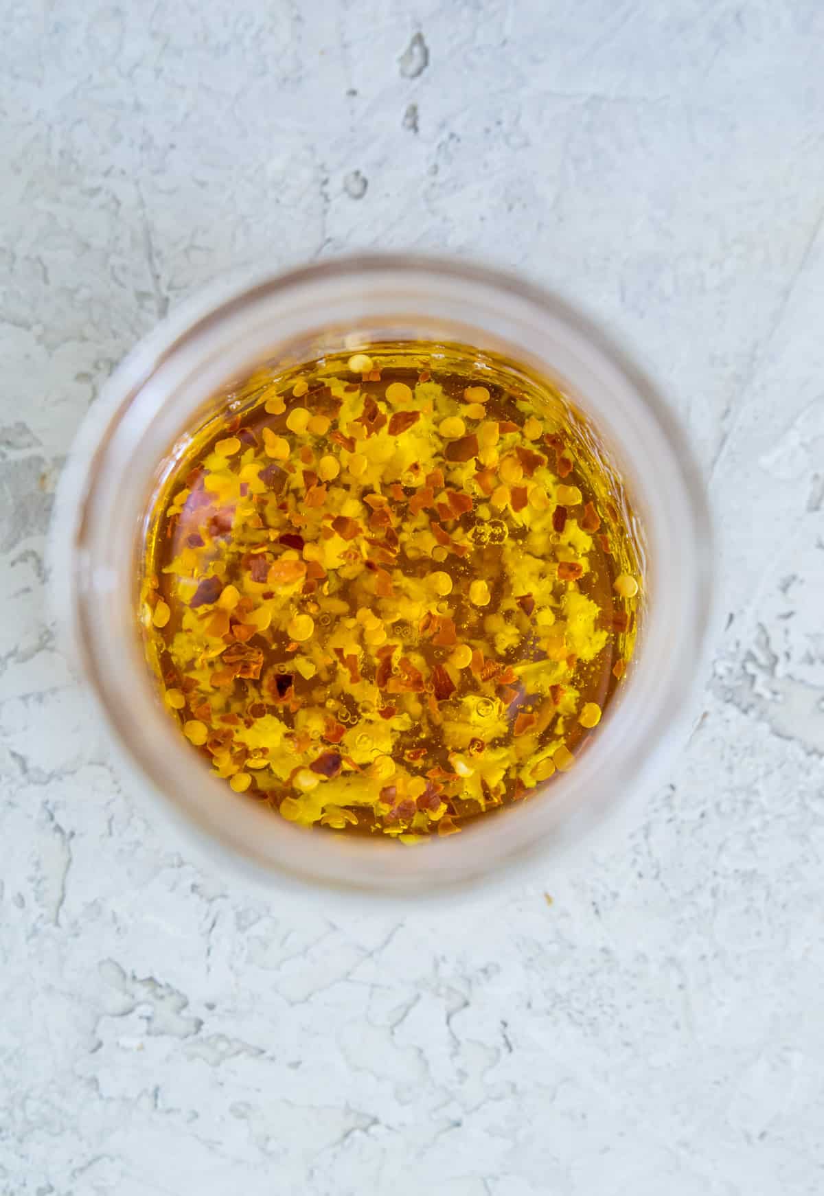 A clear jar filled with oil, spices, and chili flakes. 