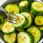 A bowl of asian cucumber salad topped with chili flakes and with a spoon in it.