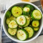 A bowl of Din Tai Fung cucumber salad topped with chili flakes and with a spoon beside it.