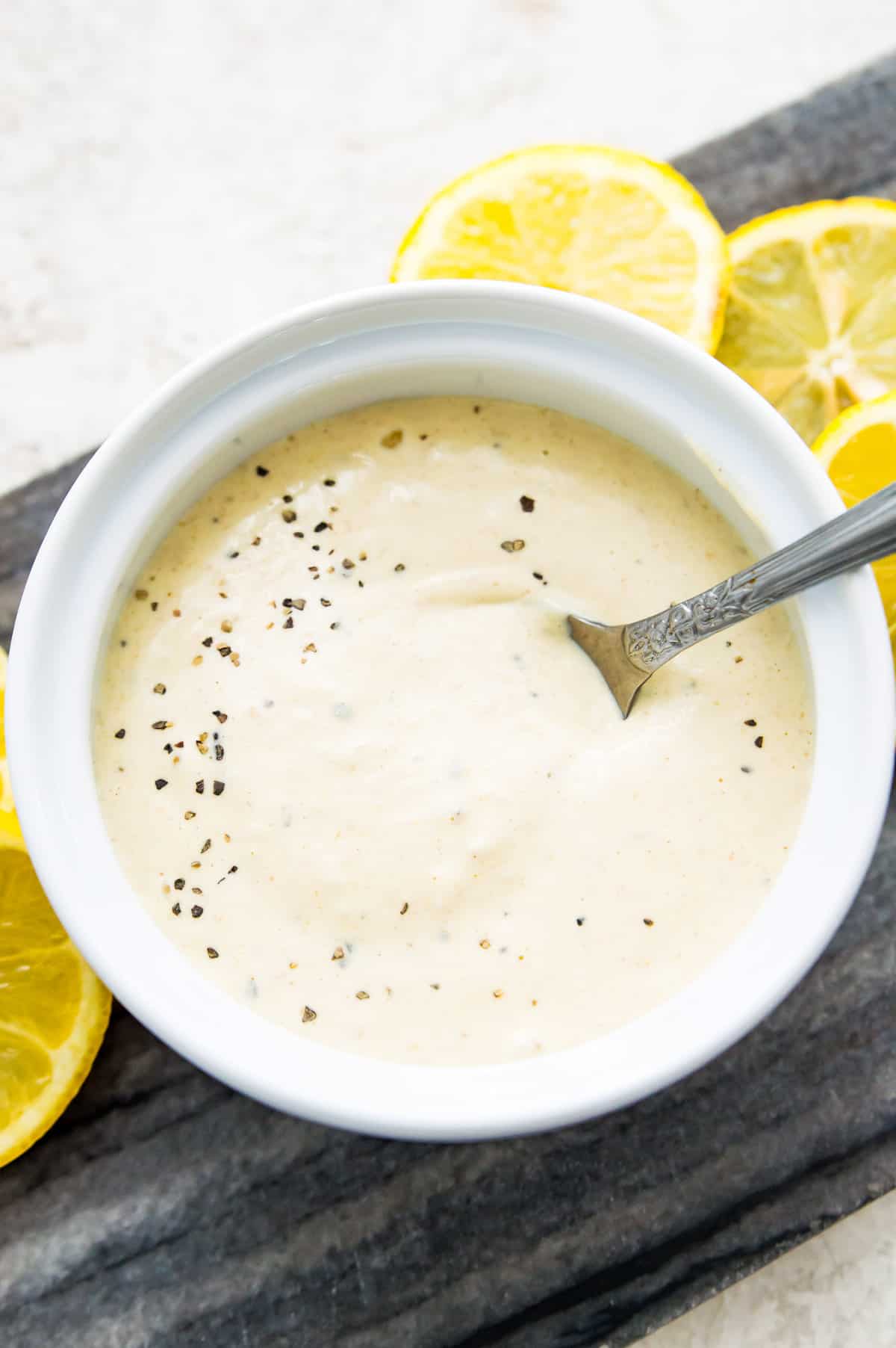 A bowl of horseradish aioli with a spoon in it, surrounded by lemon slices.