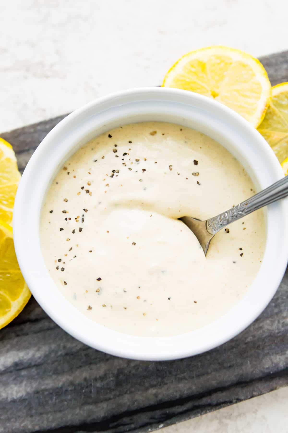A bowl with horseradish mayonnaise in it with a spoon in it and surrounded by lemon slices. 