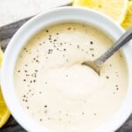 A bowl of horseradish aioli with a spoon in it surrounded by lemon slices.
