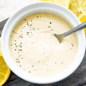 A bowl of horseradish aioli with a spoon in it surrounded by lemon slices.