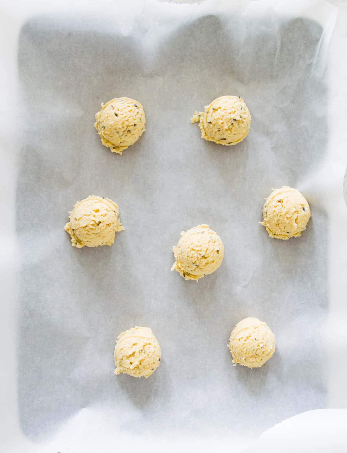 Scoops of raw cookie dough on a baking sheet lined with parchment paper.