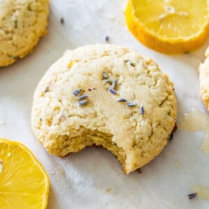 A lemon lavender cookie on a baking sheet with a bite out of it and surrounded by lemon slices.