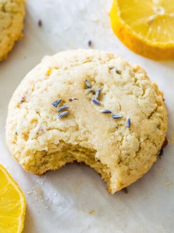 A lemon lavender cookie on a baking sheet with a bite out of it and surrounded by lemon slices.