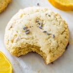 A lemon lavender cookie on a baking sheet with a bite out of it and with lavender flowers on top.
