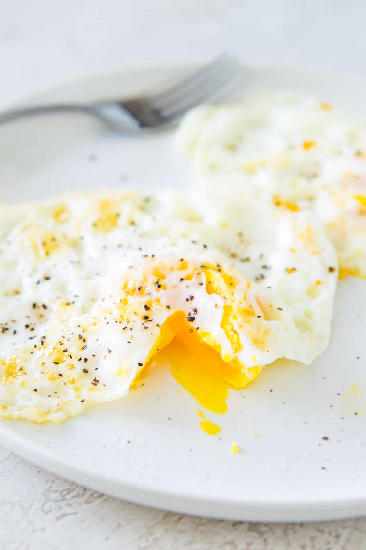 An over medium cooked egg on a plate with part of the yolk cut open.