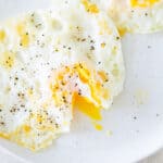 Two over medium eggs on a plate and one of them has the yolk cut open.