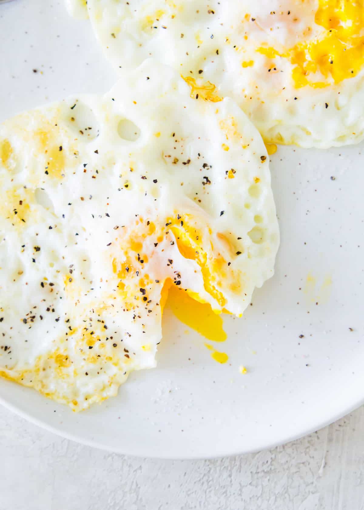 Two over medium eggs on a palate garnished with salt and pepper.